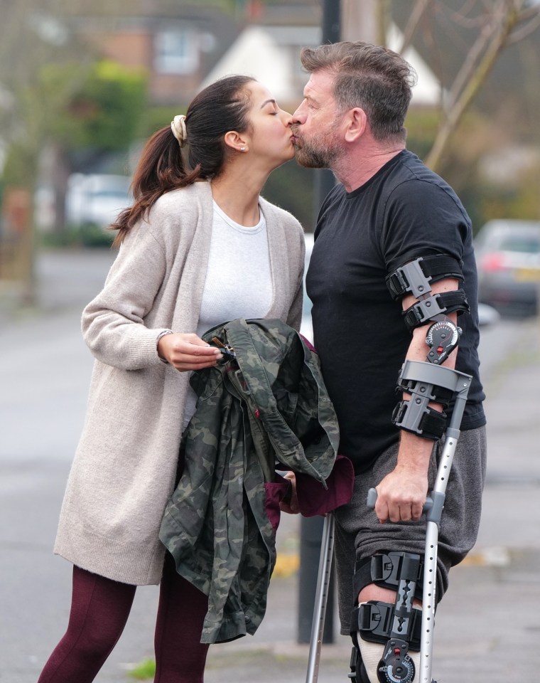 Nick Knowles and his fiancée kissing outside their home; he is using crutches and a knee brace following a knee injury.