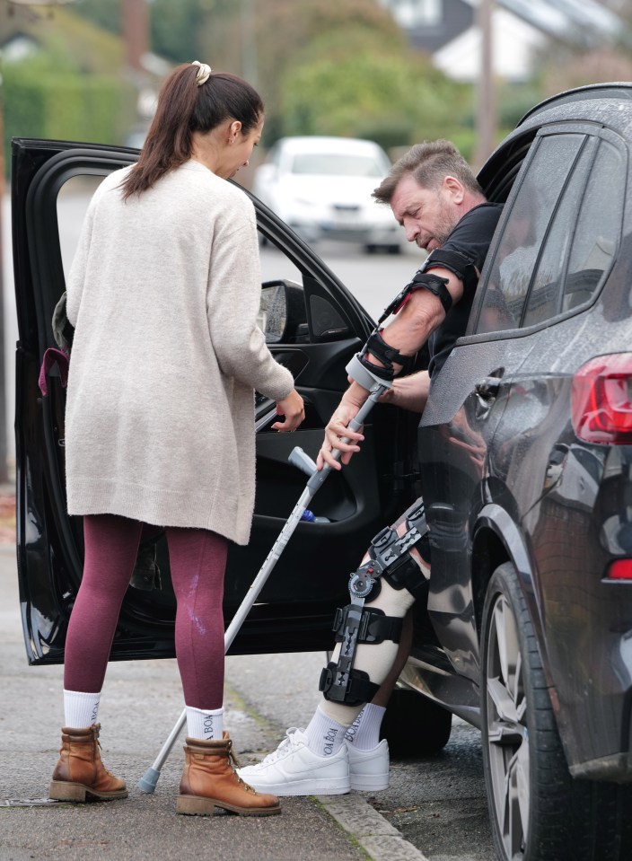 Nick Knowles, using crutches and a knee brace, exits a car with assistance.