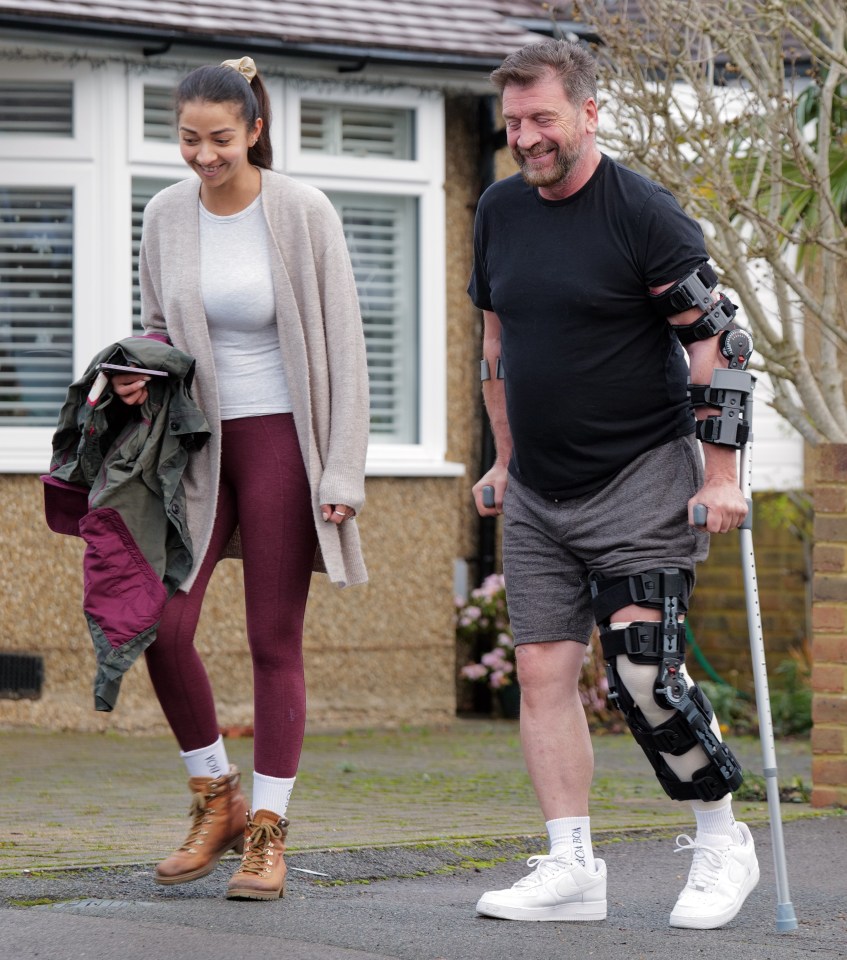 Nick Knowles, wearing a knee brace and using crutches, is helped home by his fiancée after a knee operation.