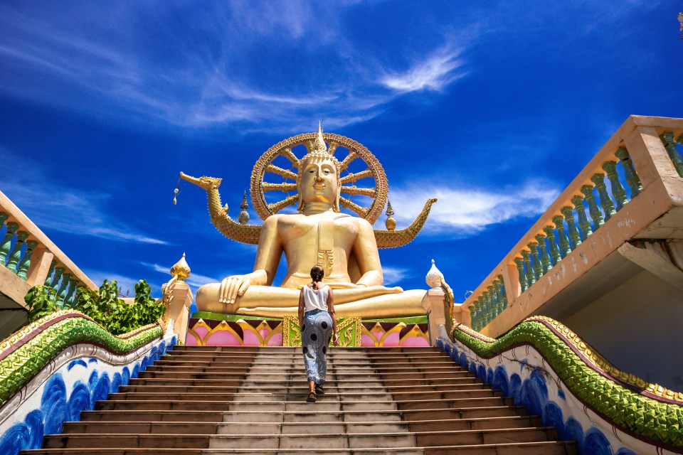 Woman ascending stairs to a large golden Buddha statue.