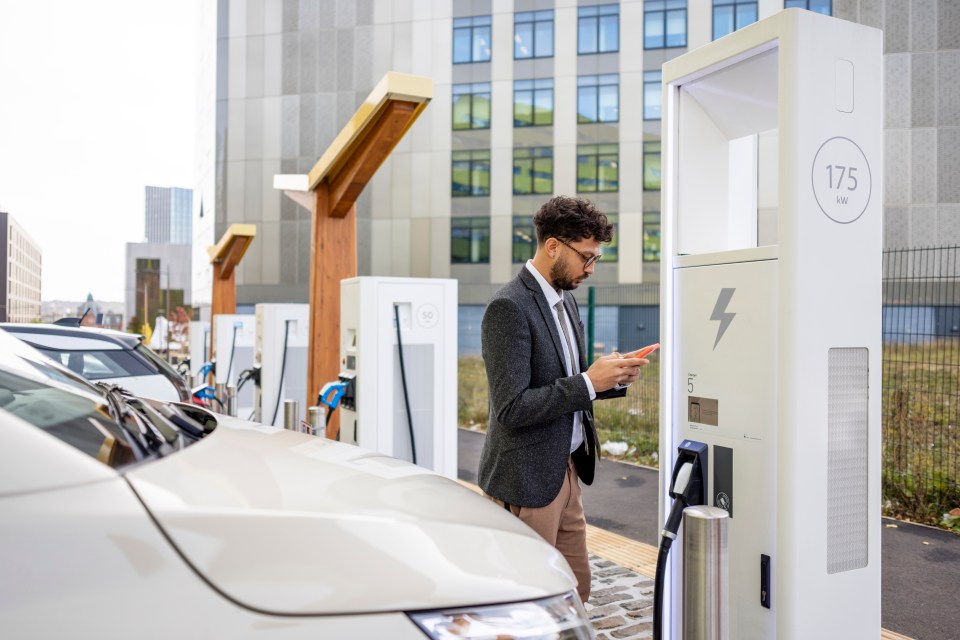 Man using phone app to charge electric vehicle at city charging station.