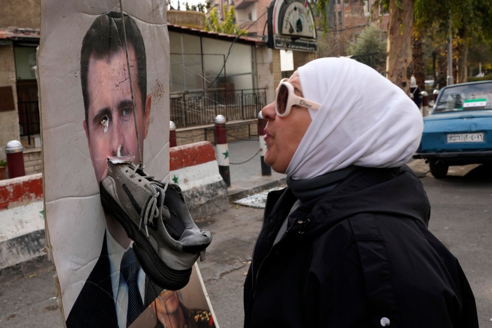 A woman spits on a portrait of ousted Syrian President Bashar Assad in Damascus, Syria