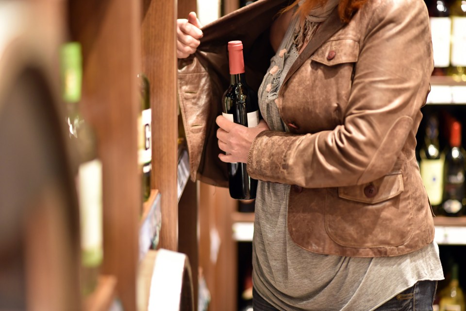 Woman shoplifting a bottle of wine.