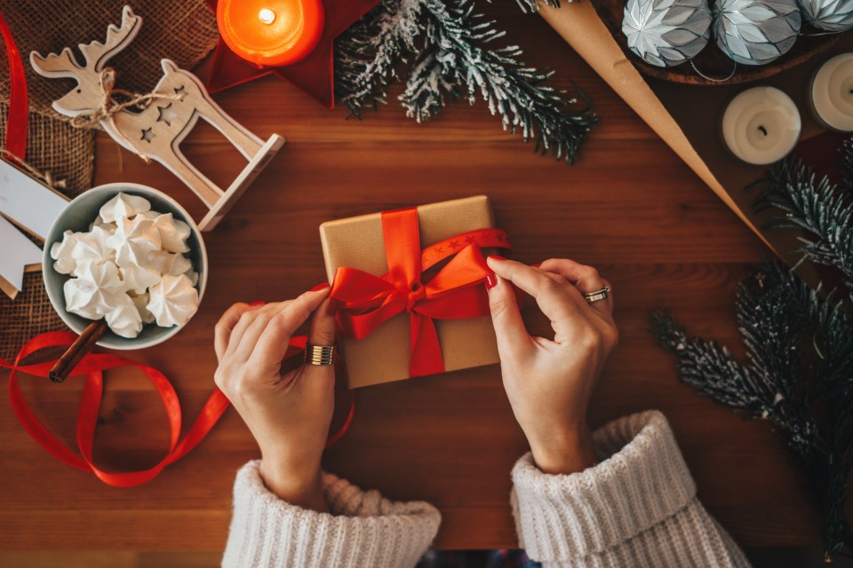 Woman tying a red ribbon on a Christmas gift.