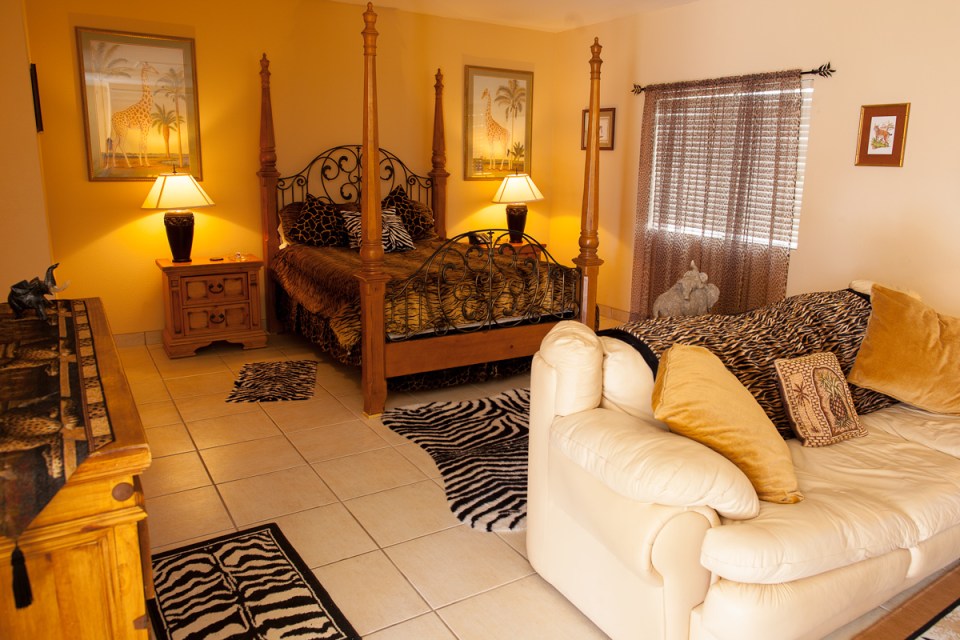 Bedroom with four-poster bed and animal print bedding, and off-white couch with animal print throw pillows and blankets.