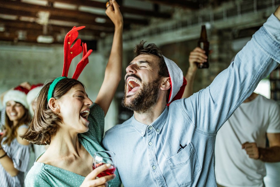 Young happy couple having fun while singing and drinking wine on New Year’s party at casual office.