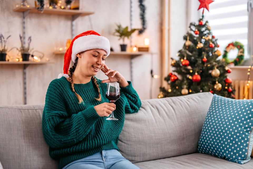 Woman in Santa hat relaxing on sofa with wine at Christmas.