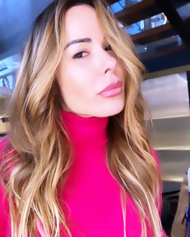 Woman with long blonde hair wearing a pink turtleneck.