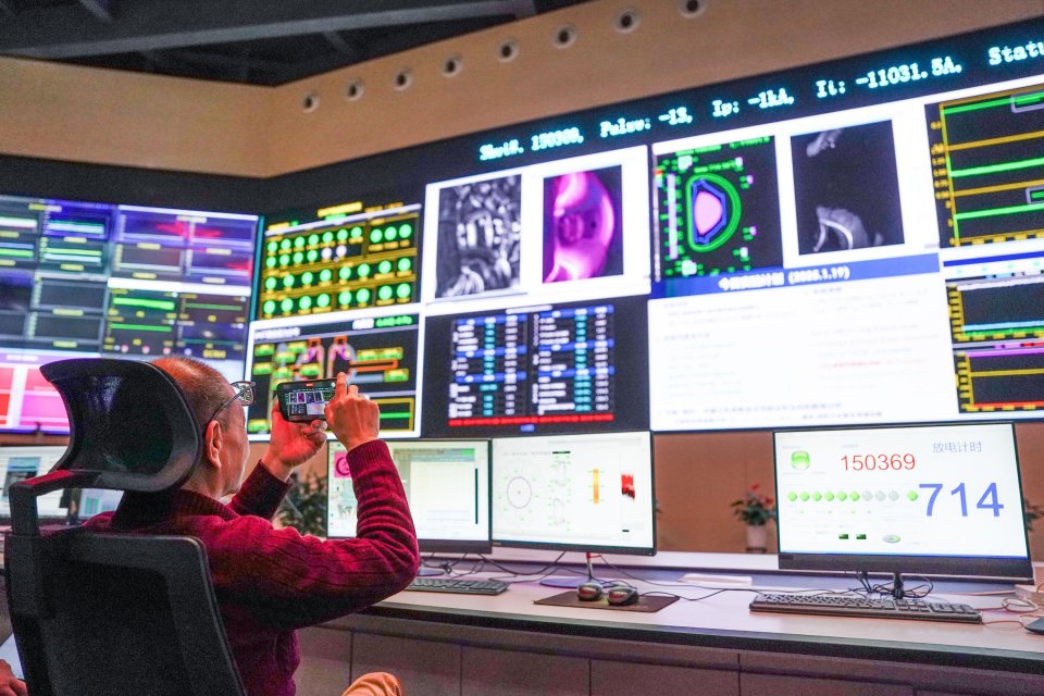 A person photographs data from a control room displaying information about a fusion energy experiment.