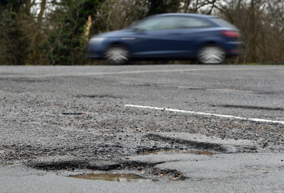 Potholes in a road with a blurred car in the background.