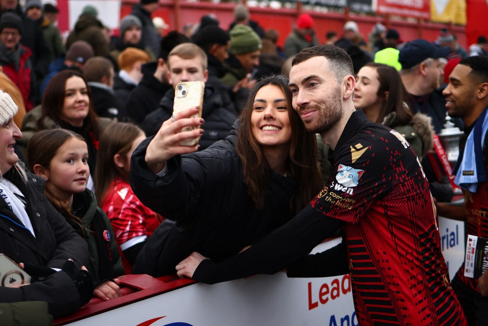 A woman and Tamworth's Tom McGlinchey take a selfie with fans after a football match.