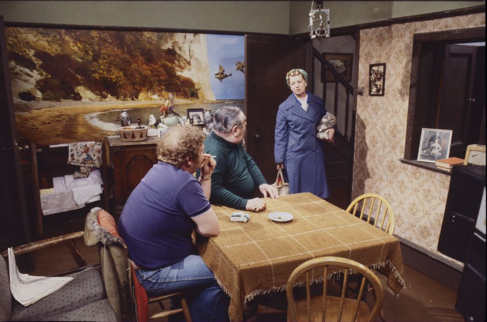 Scene from Coronation Street (1979) showing three actors seated at a kitchen table.