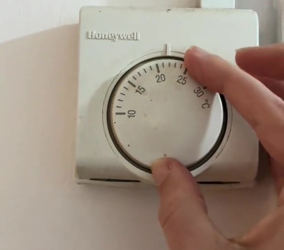 Hand adjusting a Honeywell thermostat.