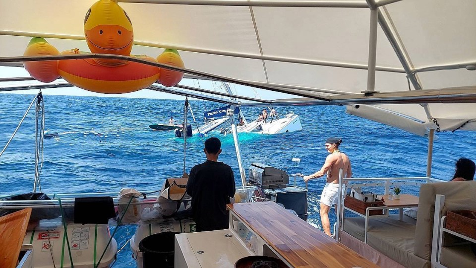 A catamaran sinking in the ocean, viewed from another boat.