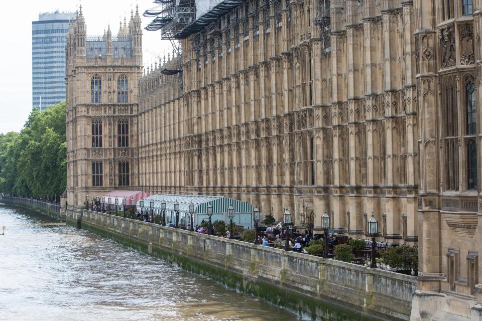 Houses of Parliament terrace with people seated at outdoor tables along the Thames River.