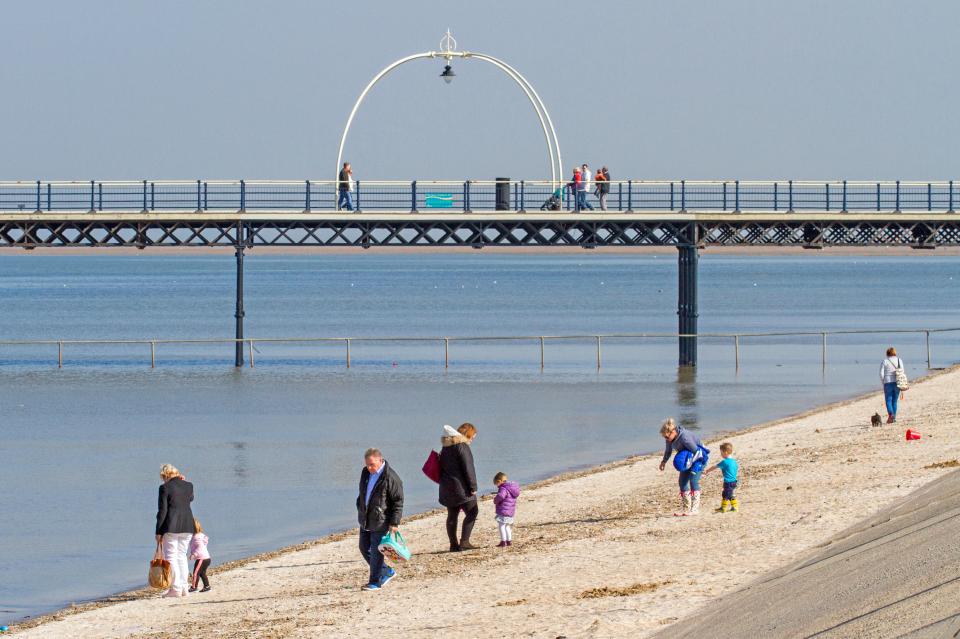 Families enjoying a sunny day at the beach with a pier in the background.