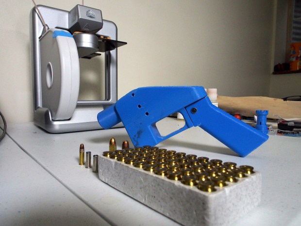 3D-printed gun next to a 3D printer and bullets.