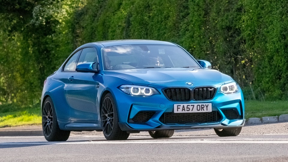 Blue BMW M2 Competition driving on a road.