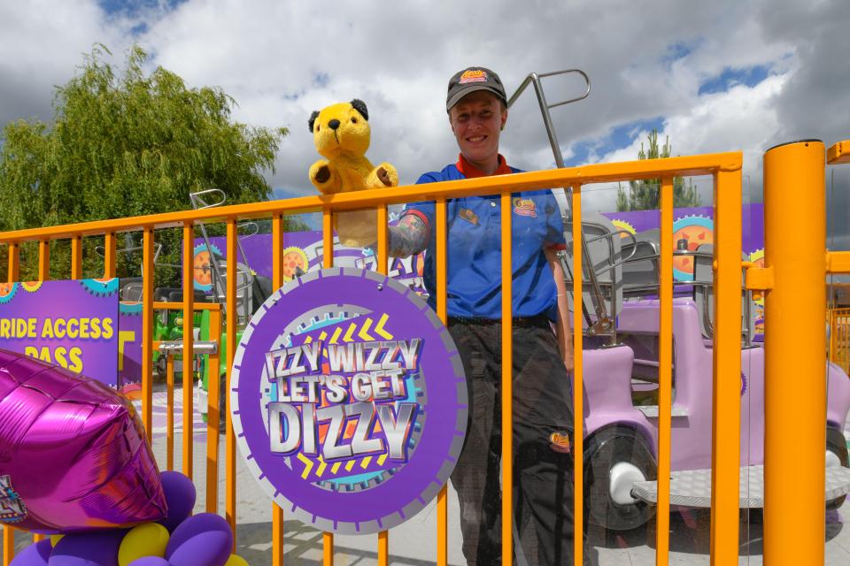 A theme park employee stands by a new ride, holding a Sooty puppet.