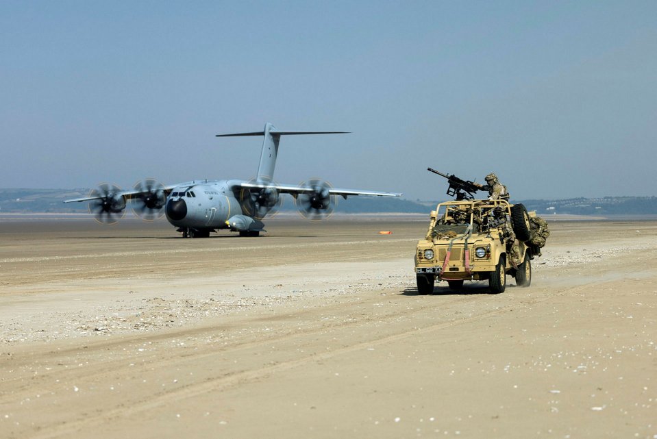 British soldiers in a Land Rover driving on a beach after exiting a C-130 transport plane.