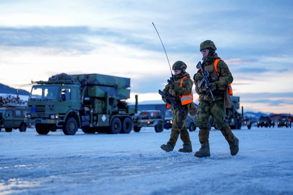 Two soldiers carrying rifles walk in the snow.