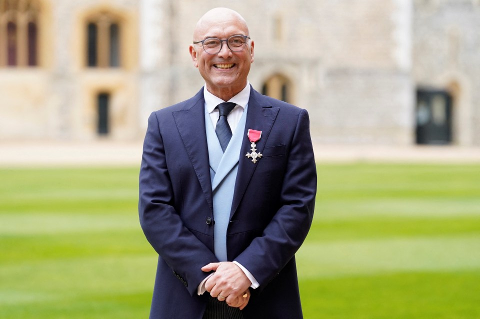 Gregg Wallace, wearing a suit and OBE medal, smiles at Windsor Castle.