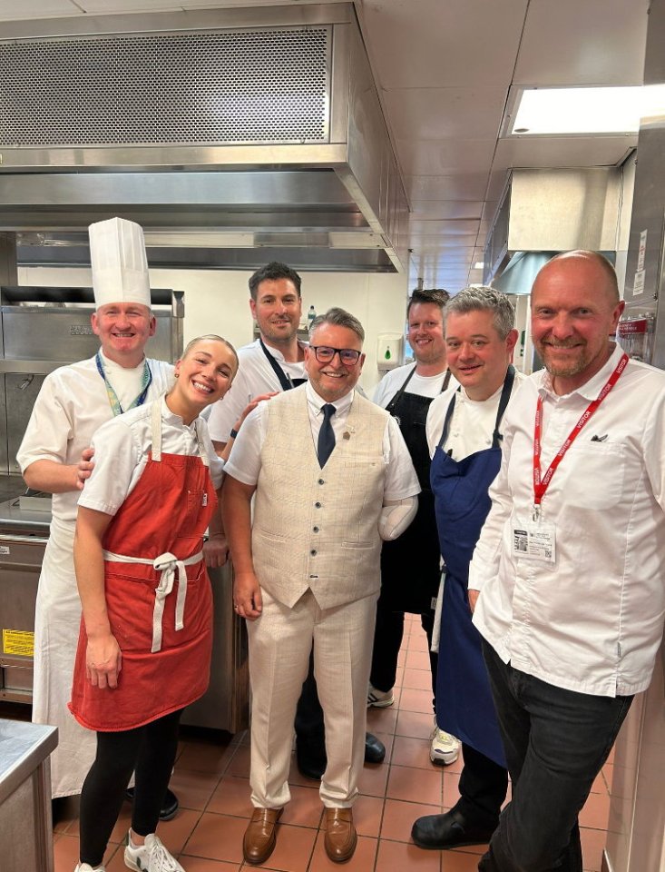 Chef posing with colleagues in a restaurant kitchen, seven years after a workplace accident resulted in an arm amputation.