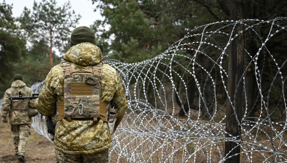 Ukrainian border guards patrol near barbed wire fence.