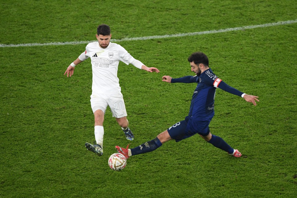 Arsenal's Jorginho in a white kit challenged by Manchester United's Bruno Fernandes during a soccer match.