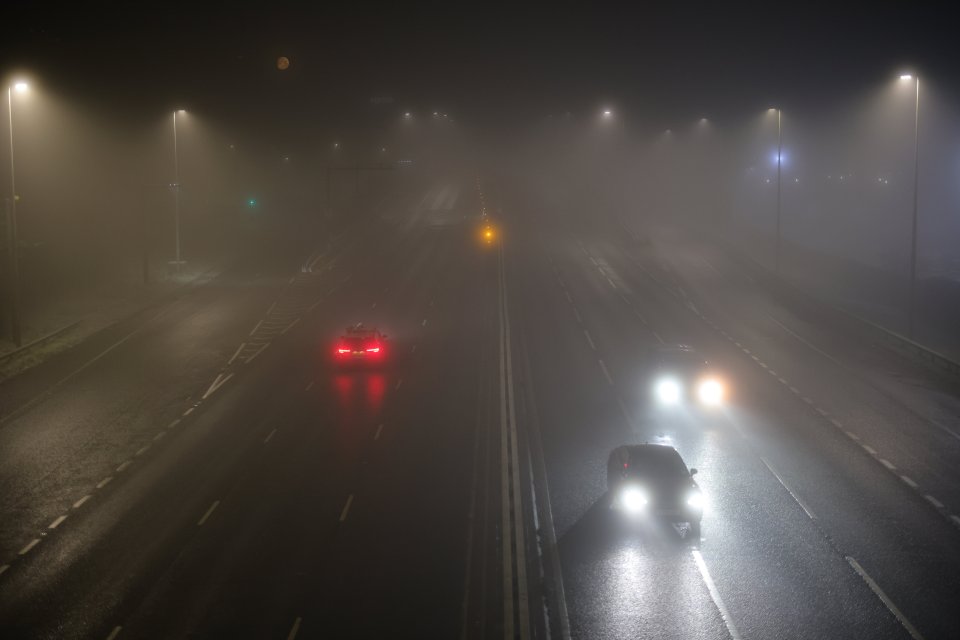 Cars driving on a foggy highway at night.