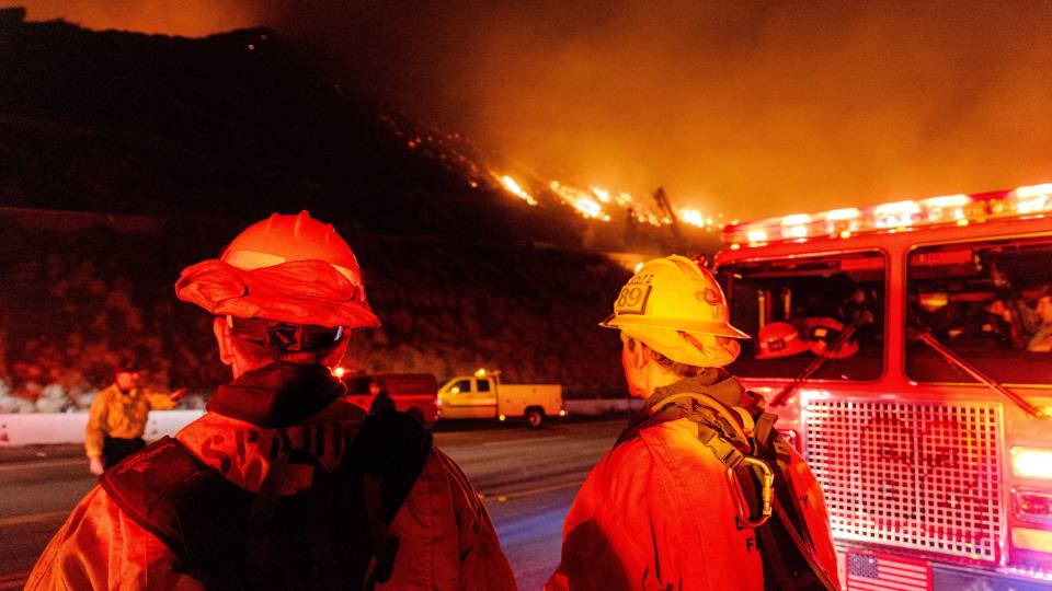 Firefighters observing a hillside fire at night.