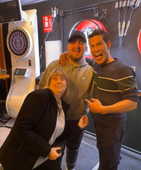 World darts champion Luke Littler with fans at a darts tournament.