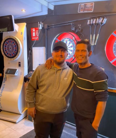 Darts world champion Luke Littler with a fan at a darts tournament.