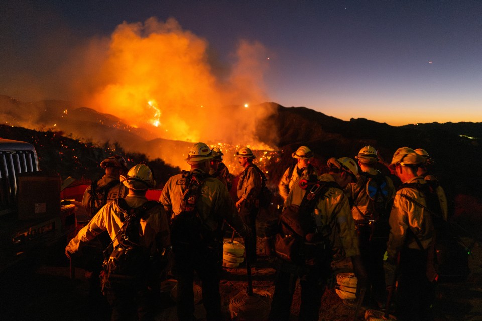 Firefighters battling a large wildfire at night.