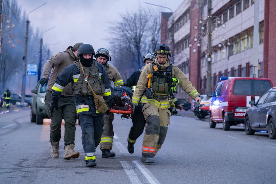 Emergency responders carry an injured person on a stretcher after a missile strike.