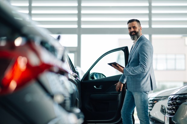 Man in a blue suit examines a car's interior at a dealership.