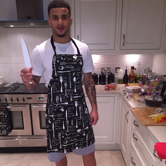 Kyle Walker in his kitchen, wearing an apron and holding a knife.