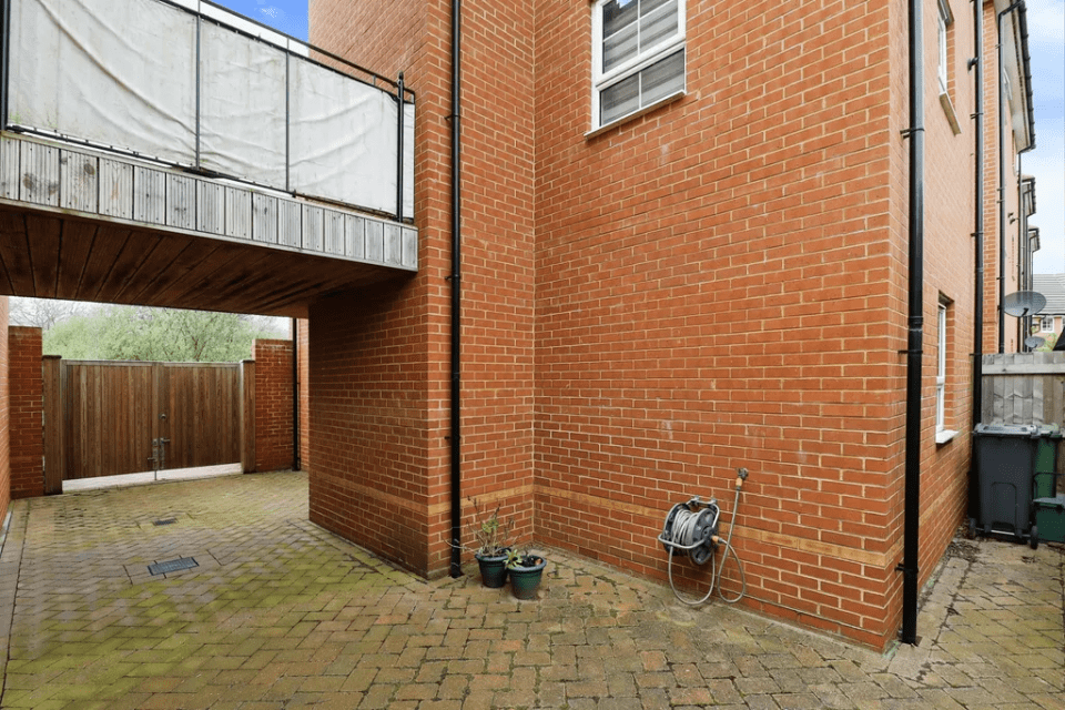 Rear patio of a brick house with a wooden gate and covered walkway.