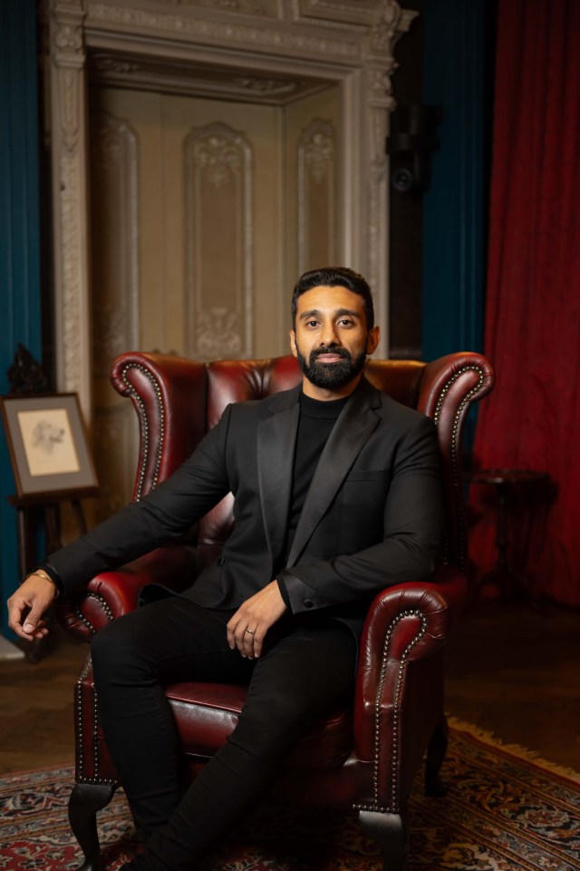 Man in black suit sitting in a leather armchair.