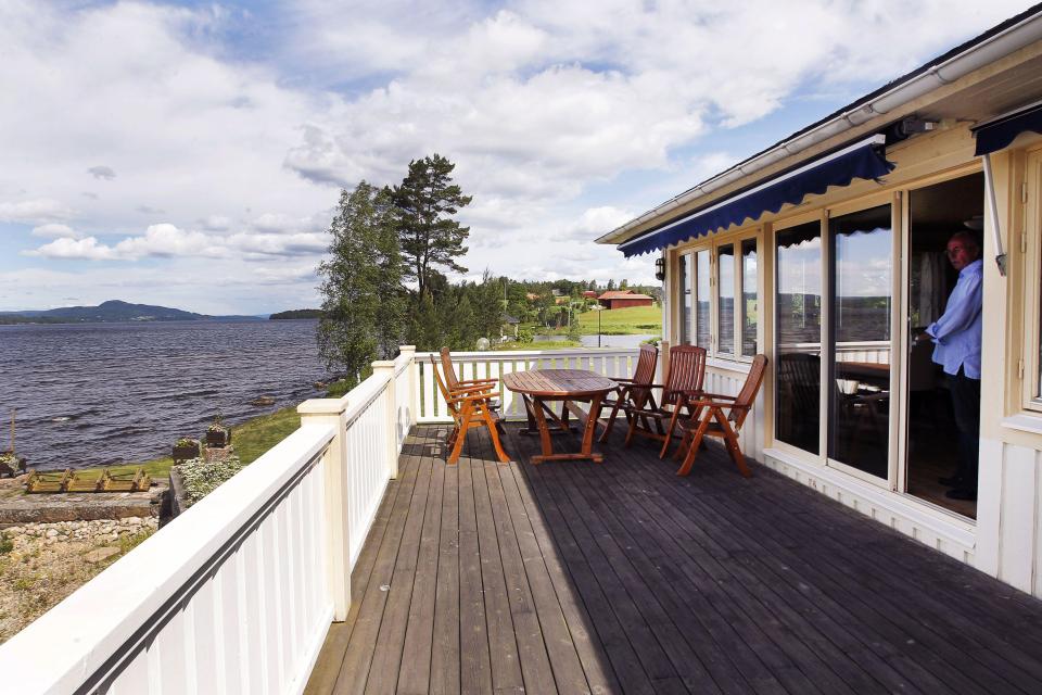 Man standing in doorway of lakeside home with patio furniture.