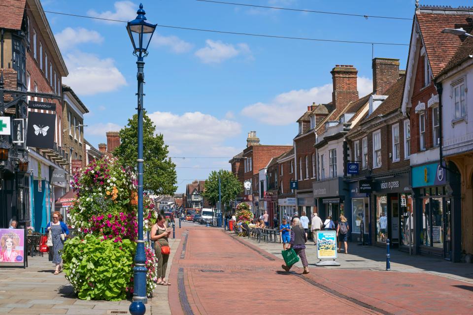 Pedestrians and shops on a sunny high street.