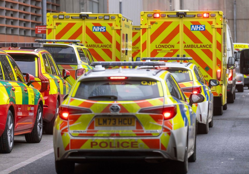 Line of NHS ambulances and police cars outside a hospital.