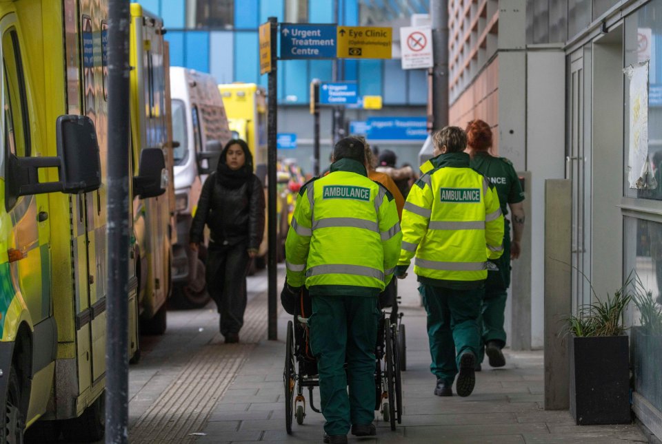 NHS paramedics wheeling a patient in a wheelchair outside a hospital.