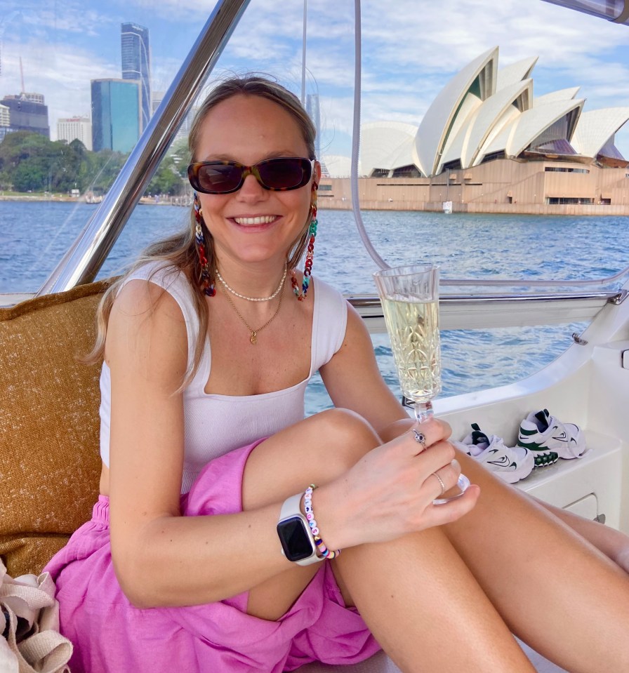 Woman on boat with champagne, Sydney Opera House in background.