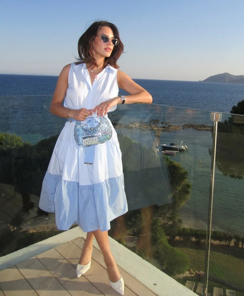 Woman in a light blue dress on a balcony overlooking the sea.