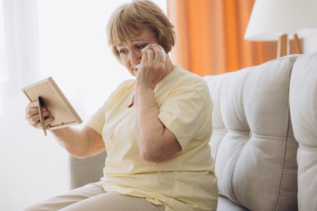 A grieving elderly woman cries while looking at a family photo.