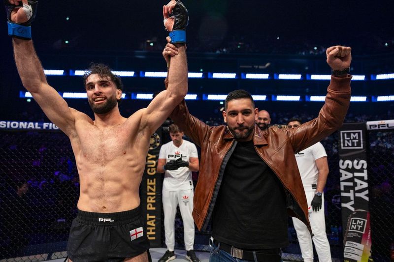 MMA fighter raising his arms in victory with his coach.