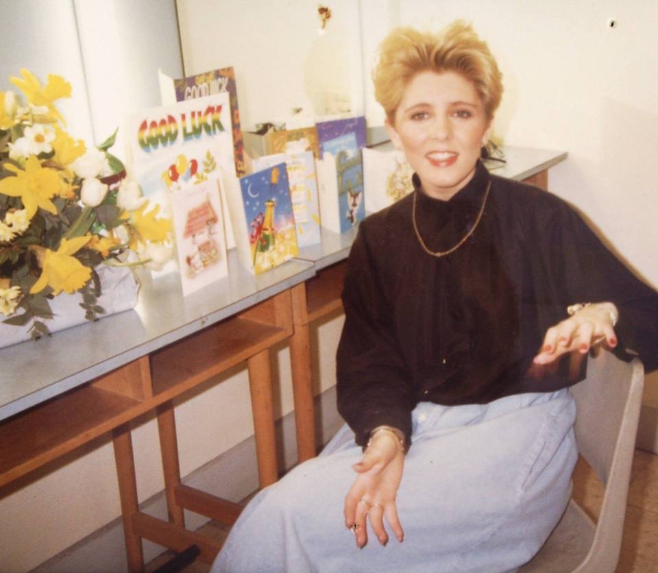 Woman sitting in chair with flowers and greeting cards on a table.