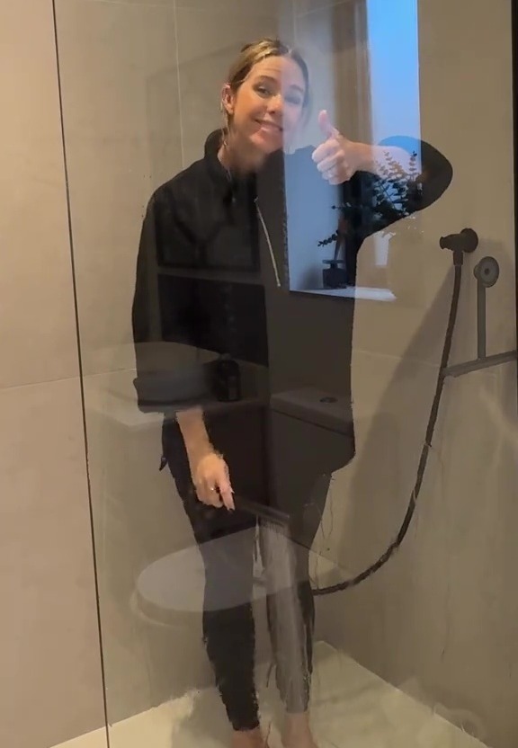 Woman in a shower giving a thumbs up while cleaning the glass door.