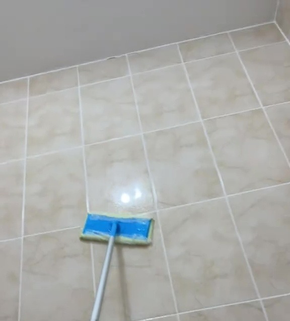 Cleaning bathroom tiles with a bleach solution and a flat mop.